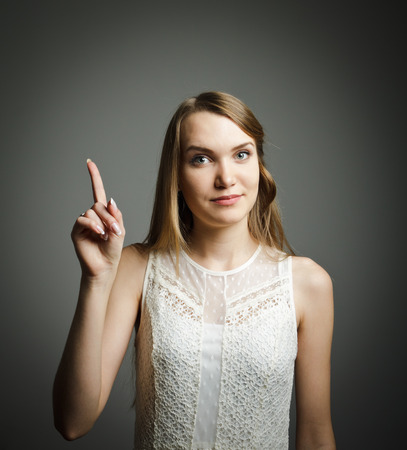 Girl in white pointing at something interesting on grey background.の写真素材