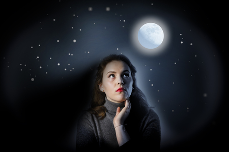 Girl in grey is looking at full moon. Girl full of doubts and hesitationの写真素材