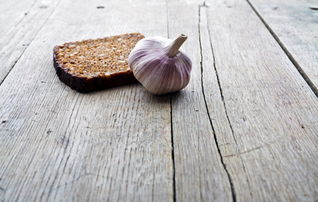 Slice of whole grain brown bread and pungent garlic on wooden table.の写真素材
