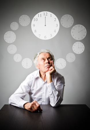 Old man in white is full of doubts and hesitation. Time and day concept. Time is passing.の写真素材