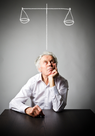 Old man in white is full of doubts and hesitation. Scales concept.の写真素材