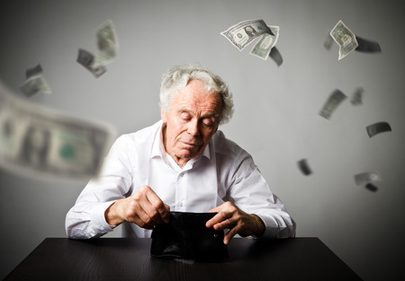 Old man in white and empty wallet. Accounting and taxes concept. Falling dollars.の写真素材