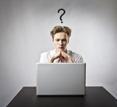 Young man using a laptop to browse the net. Question, ignorance and trouble concept.の写真素材