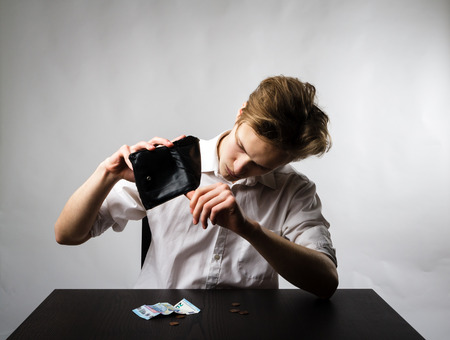 Worried young man in white is looking at an empty wallet.