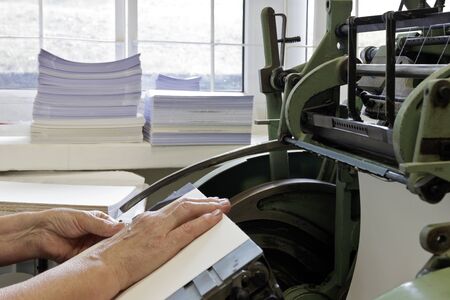 Machine for stitching book pages with threads in typography. Machine for sewing books and notebooks with threads. Women at work.の写真素材