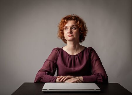 Red-haired woman using a laptop to browse the net. Sad woman.の写真素材