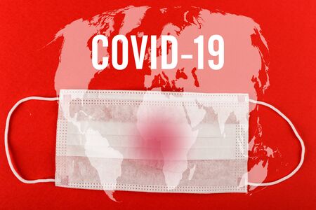 Medical protective mask on red background with COVID-19 text and World map. Surgical face mask. coronavirus outbreak concept.の写真素材