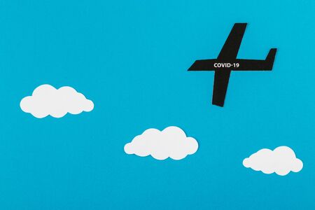 Paper airplane and coronavirus outbreak. Small paper airplane and text about COVID-19 on blue paper background. Traveling during the COVID-19 pandemic.の写真素材