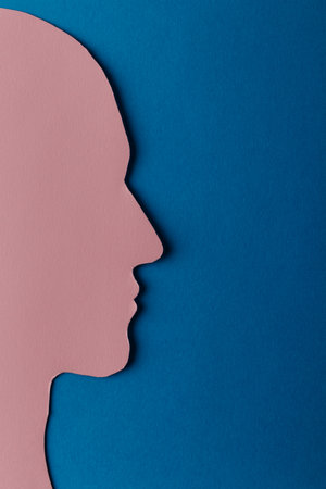 Head silhouette made of paper. Pink paper shaped as a human head with copy space on blue paper background. Minimal concept.の写真素材