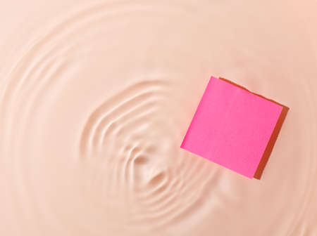 Pink sticky note in water on wavy background.