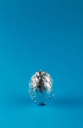 Egg in aluminum foil on blue background with copy space. Space travel and food concept. One egg.の写真素材