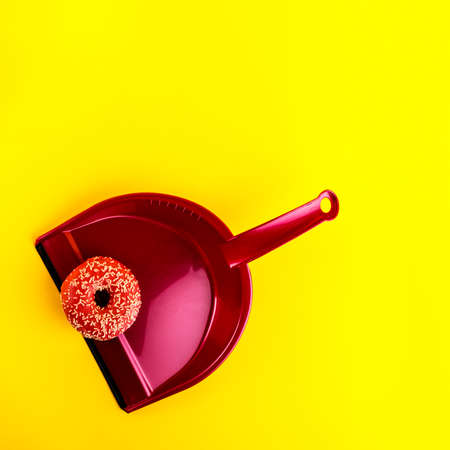 Pink dust pan with sprinkled pink donut on yellow background. Sweet and junk food.の写真素材