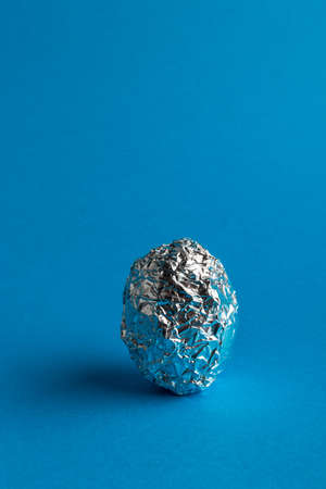 Egg in aluminum foil on blue background with copy space. Easter symbol and sign. One egg.