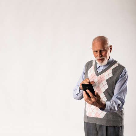 Old man is using a smart phone on gray background with copy space. Communication.の写真素材