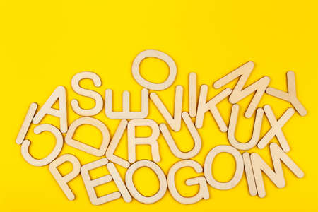 Wooden alphabet letters on yellow paper background. A lot of wooden letters with copy space. Chaos...