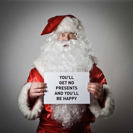 Santa Claus is holding white paper with wishes and congratulations. Black plain text on white paper: You'll Get No Presents and you'll be happy. The Great Reset concept.の写真素材