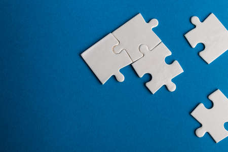 White jigsaw puzzle pieces on blue background. Texture photo with space for text. Teamwork conceptual photo.の写真素材