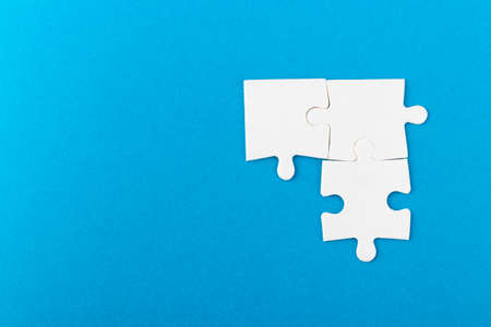 White jigsaw puzzle pieces on blue background. Texture photo with space for text. Teamwork conceptual photo.の写真素材