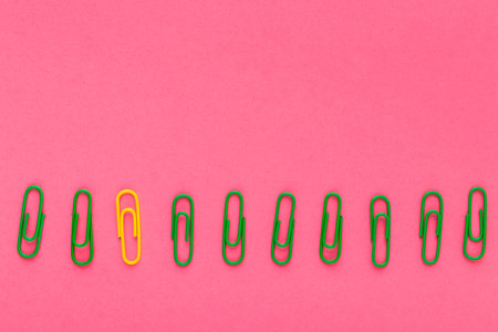 Colored paper clips. Green and yellow paper clips macro close up isolated on a pink background with copy space.の写真素材