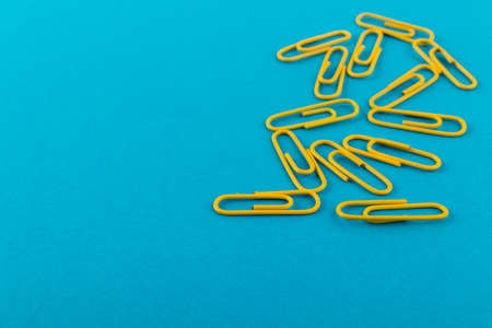 Colored paper clips. Yellow paper clips macro close up isolated on a blue background with copy...