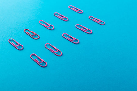 Colored paper clips. Pink paper clips macro close up isolated on a blue background with copy space.の写真素材