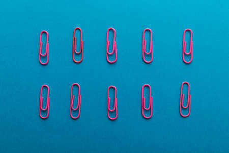 Colored paper clips. Pink paper clips macro close up isolated on a blue background with copy space.