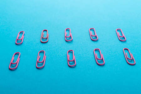 Colored paper clips. Pink paper clips macro close up isolated on a blue background with copy space.の写真素材