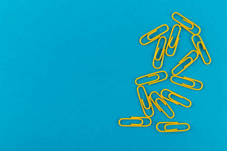 Colored paper clips. Yellow paper clips macro close up isolated on a blue background with copy space.の写真素材
