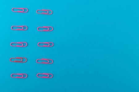 Colored paper clips. Pink paper clips macro close up isolated on a blue background with copy space.の写真素材