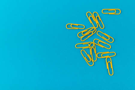 Colored paper clips. Yellow paper clips macro close up isolated on a blue background with copy space.の写真素材