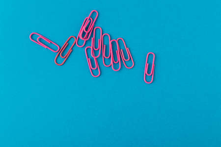 Colored paper clips. Pink paper clips macro close up isolated on a blue background with copy space.の写真素材