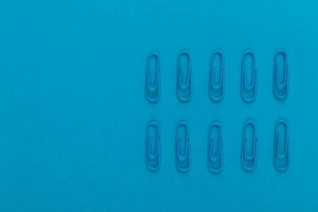Colored paper clips. Blue paper clips macro close up isolated on a blue background with copy space.の写真素材