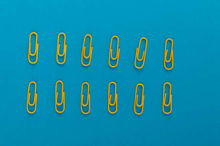 Colored paper clips. Yellow paper clips macro close up isolated on a blue background with copy space.の写真素材