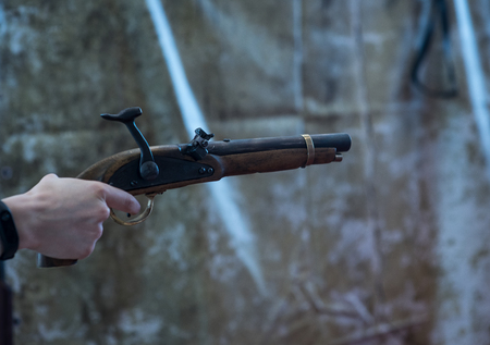Hands of man in vintage clothing holding muzzle loading musket. Before the shot