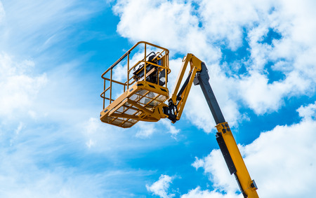 Hydraulic lift platform with bucket of yellow construction vehicle, heavy industry, blue sky and...