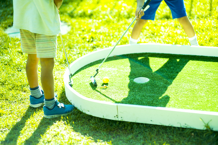 children play on the golf course.Casual kids at a golf field holding golf clubs. Sunsetの写真素材