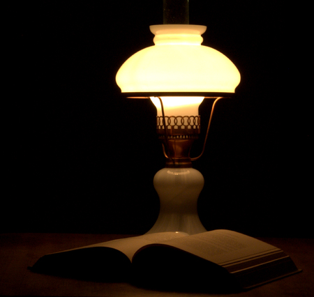 Old fashioned kerosene lantern style oil lamp burning next to the bookの写真素材