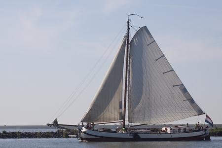 ENKHUIZEN, THE NETHERLANDS - JULY 18.2015: traditional sailing boat with hoisted sails illuminated by the sun sails out of port with people for a sailing tripのeditorial素材