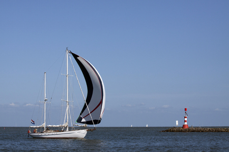 ENKHUIZEN, THE NETHERLANDS - JUNE 7, 2015: White sailboat with sails spinnaker sail fits a dam with a lighthouse at the port of enkhuizenのeditorial素材