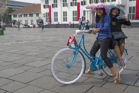 JAKARTA, JAVA, INDONESIA - AUGUST 10, 2018: Two cycling ladies with a hat on a square in Jakarta on Java.のeditorial素材