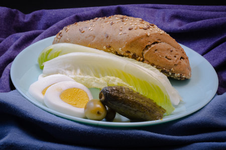 rustic bun,salad,pickles,onion and a boiled egg on a blue plateの写真素材