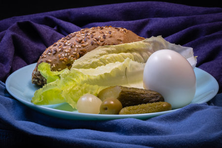 rustic bun,salad,pickles,onion and a boiled egg on a blue plateの写真素材