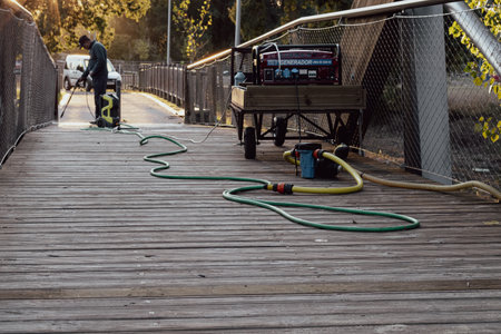 municipal employee cleaning a wooden bridge with a pressure washing machineの写真素材