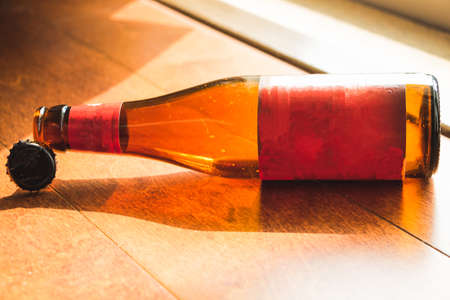 Shiny empty beer bottle lying down on wooden floor in natural lightの写真素材