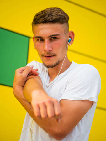 A young Caucasian man wearing earphones and working out near the bright yellow wallの写真素材