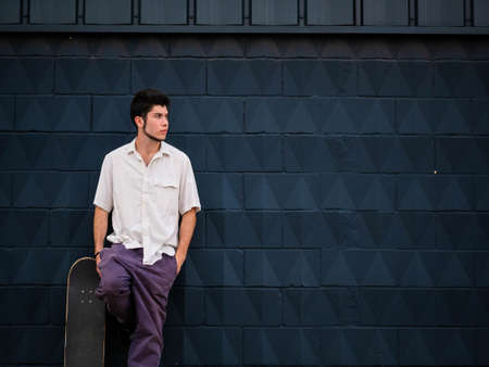 A young attractive male with skateboard posing at camera against a gray backgroundの写真素材