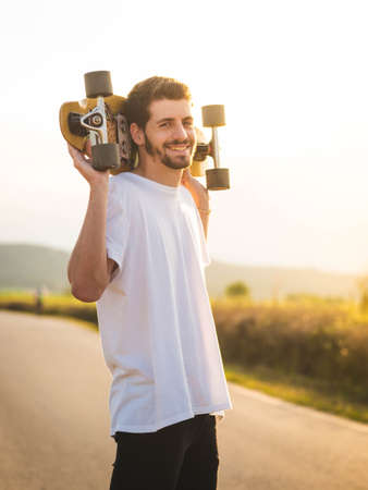 A vertical shot of a man holding a skateboard during the sunsetの写真素材