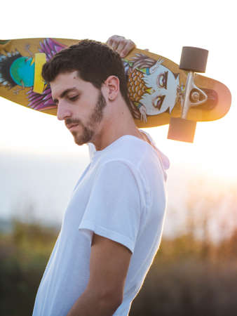 A vertical shot of a man holding a skateboard during the sunsetの写真素材