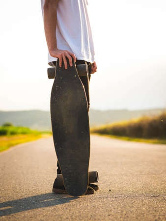 A vertical shot of a man holding a skateboard during the sunsetの写真素材