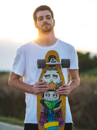 A vertical shot of a man holding a skateboard during the sunsetの写真素材